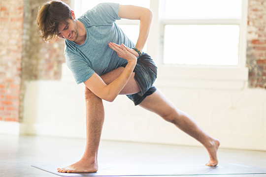 Young man doing a twisting lunge yoga pose in an open, airy yoga studio in Morristown, NJ.