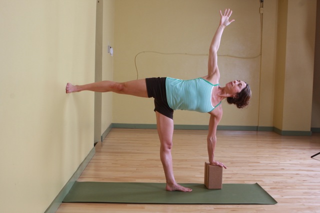 Woman pressing heel into wall during half moon pose.